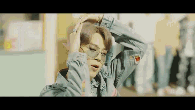 a young man wearing a denim jacket and sunglasses is holding his hair .