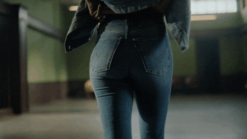 a woman in a denim jacket and jeans is walking in a dark room