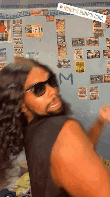 a man wearing sunglasses stands in front of a wall that says mikey 's bump n curl on it