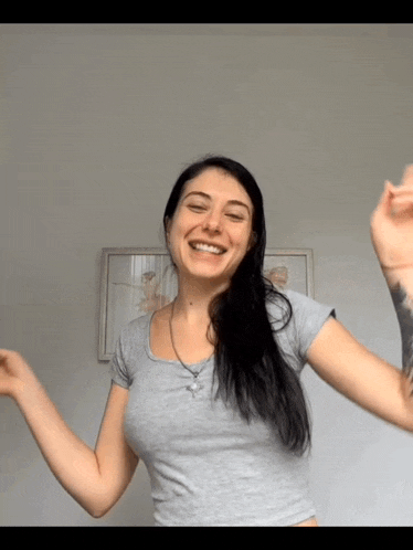 a woman in a grey shirt is smiling with her arms outstretched in front of a picture of a ballerina