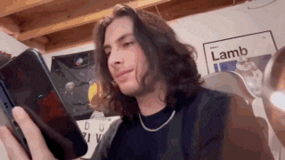 a young man with long hair is looking at his cell phone .