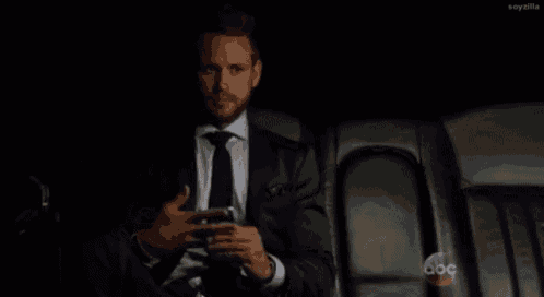 a man in a suit and tie is sitting in the back seat of a car looking at his cell phone .