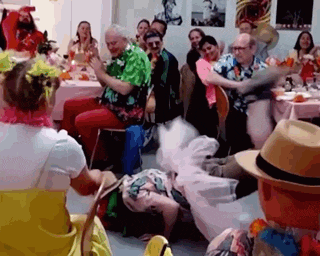 a group of people dressed in hawaiian costumes are dancing in a room at a party .