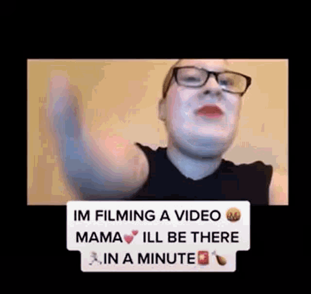 a woman wearing glasses and red lipstick is filming a video and says `` mama ill be there in a minute '' .