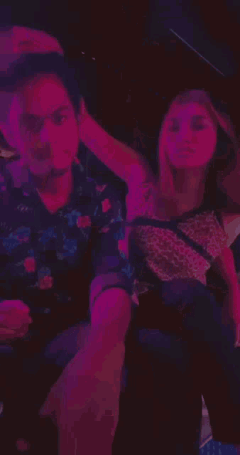 a man and a woman are posing for a picture in a dark room with purple lights behind them .