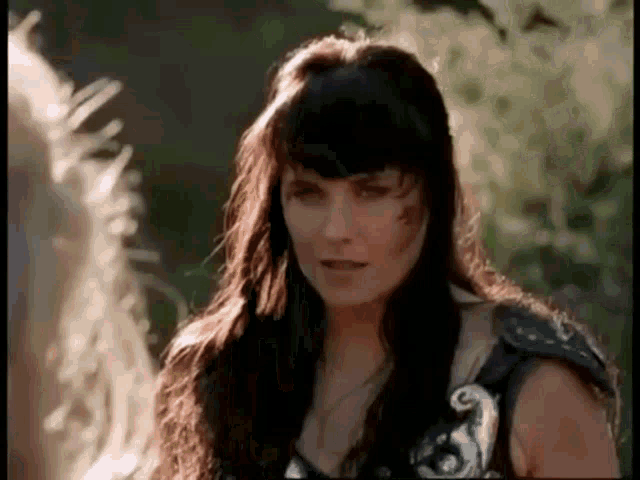 a woman with long dark hair is standing next to a horse in a field .