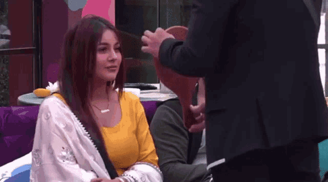 a woman in a yellow top is sitting next to a man in a suit and talking to him .