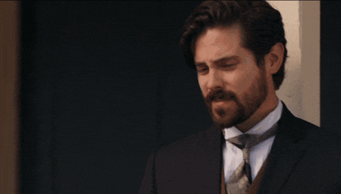 a man with a beard wearing a suit and tie stands in front of a door