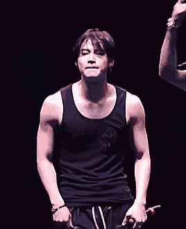 a man in a black tank top is holding a microphone while standing on a stage .