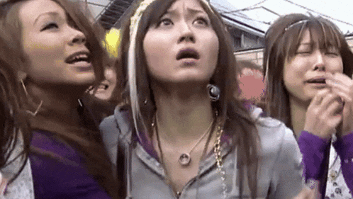 three women are standing next to each other and one of them is wearing a necklace with a circle on it .