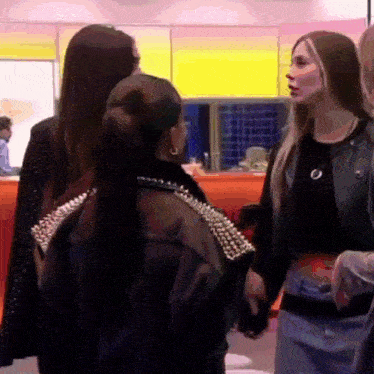 a group of women are standing next to each other in a room talking .