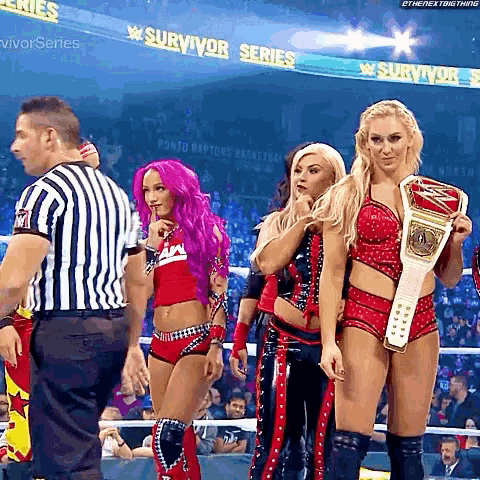 a group of women are standing in front of a referee holding a wrestling championship .