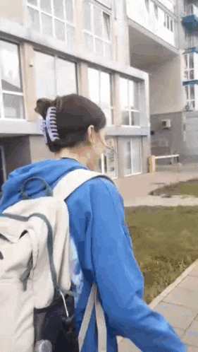 a woman wearing a blue hoodie and a backpack is walking down a sidewalk in front of a building .