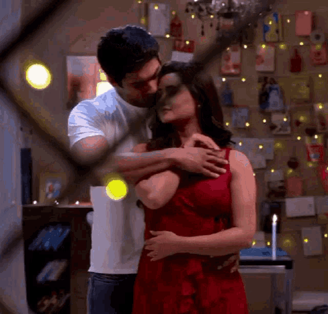 a man in a white shirt is hugging a woman in a red dress in a room .