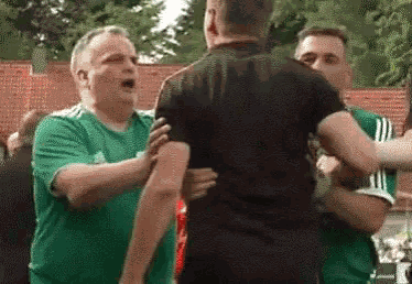 a group of men are standing next to each other and one of them is wearing a green adidas shirt .