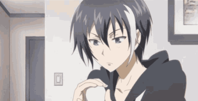 a boy with a black hoodie is holding a white object in his hand .