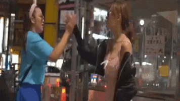 two women are giving each other a high five while standing next to each other on a city street .