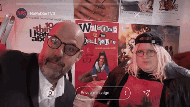 a man and a woman standing in front of a wall with a welcome to the dollhouse poster