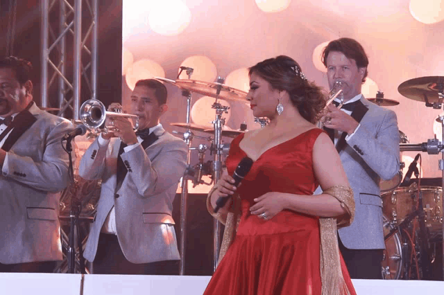 a woman in a red dress sings into a microphone while a band plays behind her