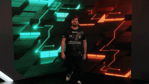 a man in a sela gaming shirt stands in front of a green and red background
