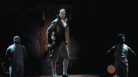 a man in a suit is dancing on a stage while two men hold his hand .