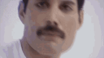 a close up of a man 's face with a mustache and a white shirt .