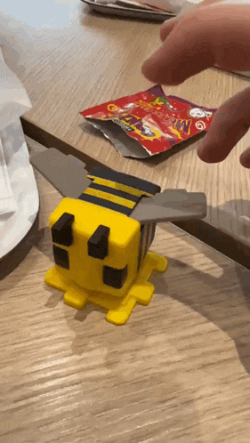 a toy bee is sitting on a table next to a bag that says ' minecraft ' on it