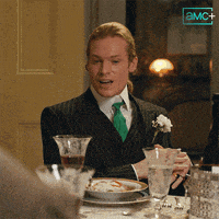 a man in a suit and tie is sitting at a table with a sign that says ' amc + ' on it