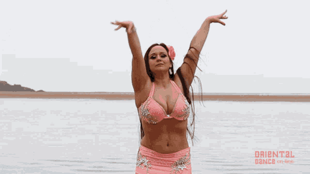 a woman in a pink bikini stands in front of a body of water with the words oriental dance on the bottom right