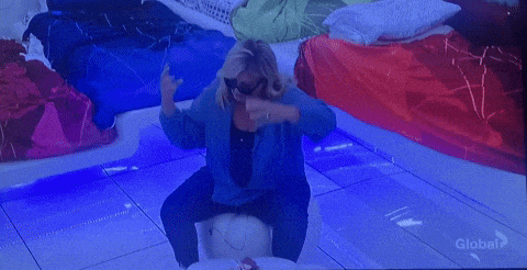 a woman wearing sunglasses is sitting on a toilet in front of a global tv screen