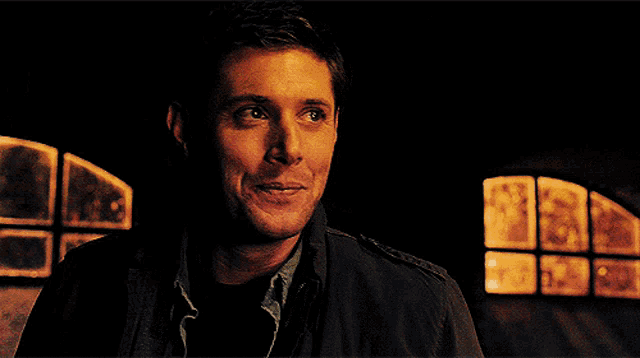 a man in a dark room with a window in the background is smiling