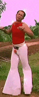 a man in a red tank top and white flared pants
