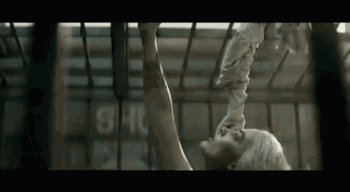 a woman is hanging upside down from a cage in a movie .