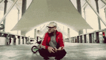 a man wearing a red adidas jacket squatting down