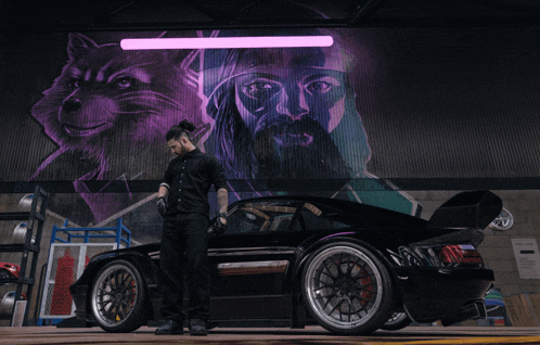 a man is standing in front of a car with a mural on the wall behind him