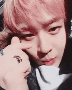 a young man with pink hair is making a heart shape with his finger .