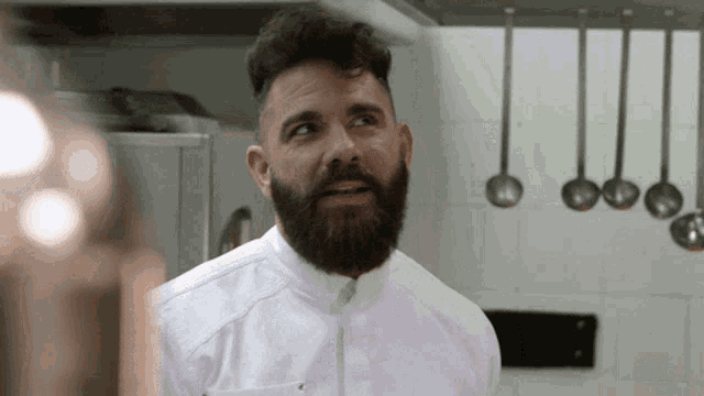 a man with a beard in a kitchen with ladles hanging on the wall