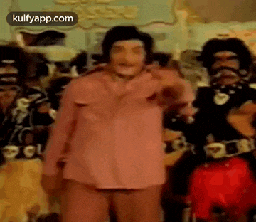 a man in a pink shirt is standing in front of a crowd of people in costume .