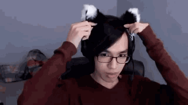 a young man wearing glasses and cat ears is sitting in a chair .
