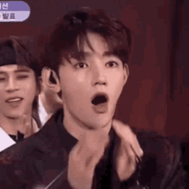 a man is covering his mouth with his hand while another man is behind him .