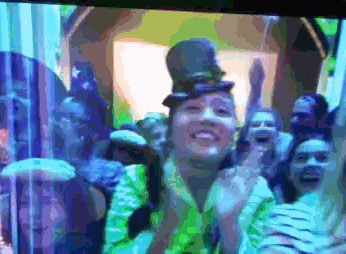 a woman wearing a top hat and a green shirt stands in front of a crowd of people