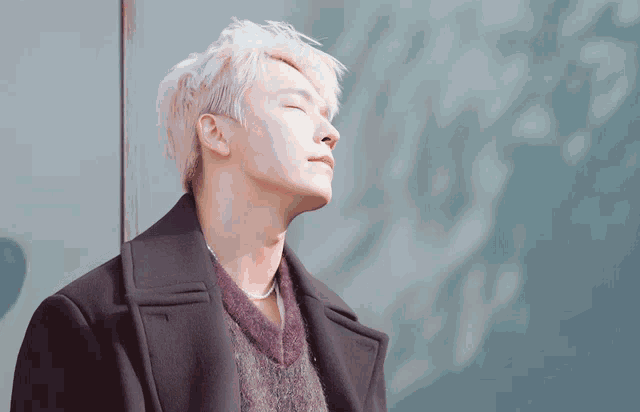 a young man with white hair is leaning against a wall