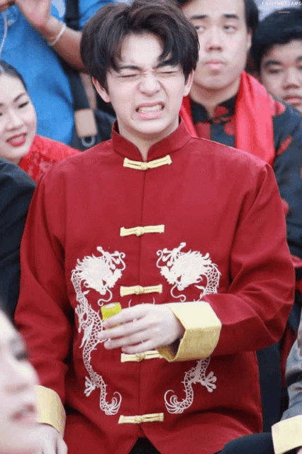 a man wearing a red jacket with dragons on it making a funny face