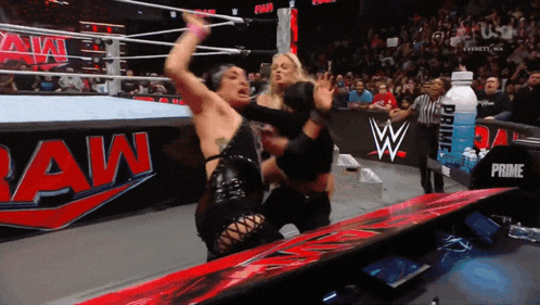 two women are wrestling in front of a sign that says raw on it