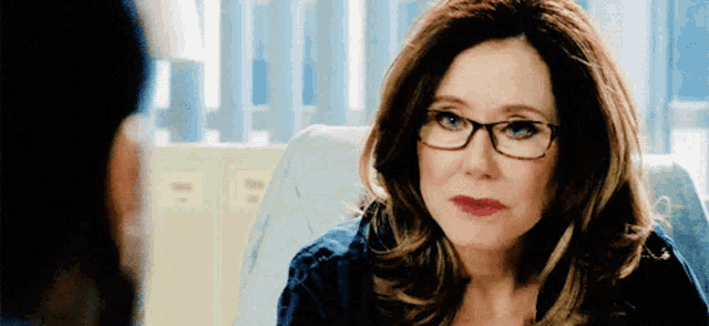 a woman wearing glasses is sitting in a chair and looking at the camera