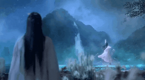 a woman in a white dress is standing in front of a waterfall in a forest .