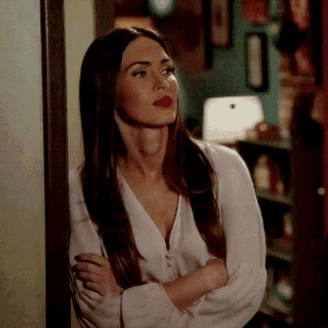 a woman wearing a white shirt and red lipstick stands with her arms crossed