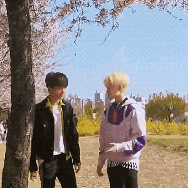 two young men standing next to each other under a tree in a park