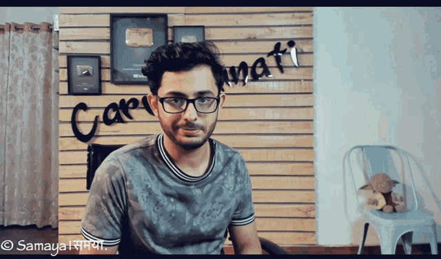a man wearing glasses is sitting in front of a wall that says ' carpati ' on it