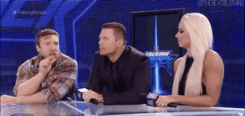 a man and a woman are sitting at a table talking to each other on a wrestling show .